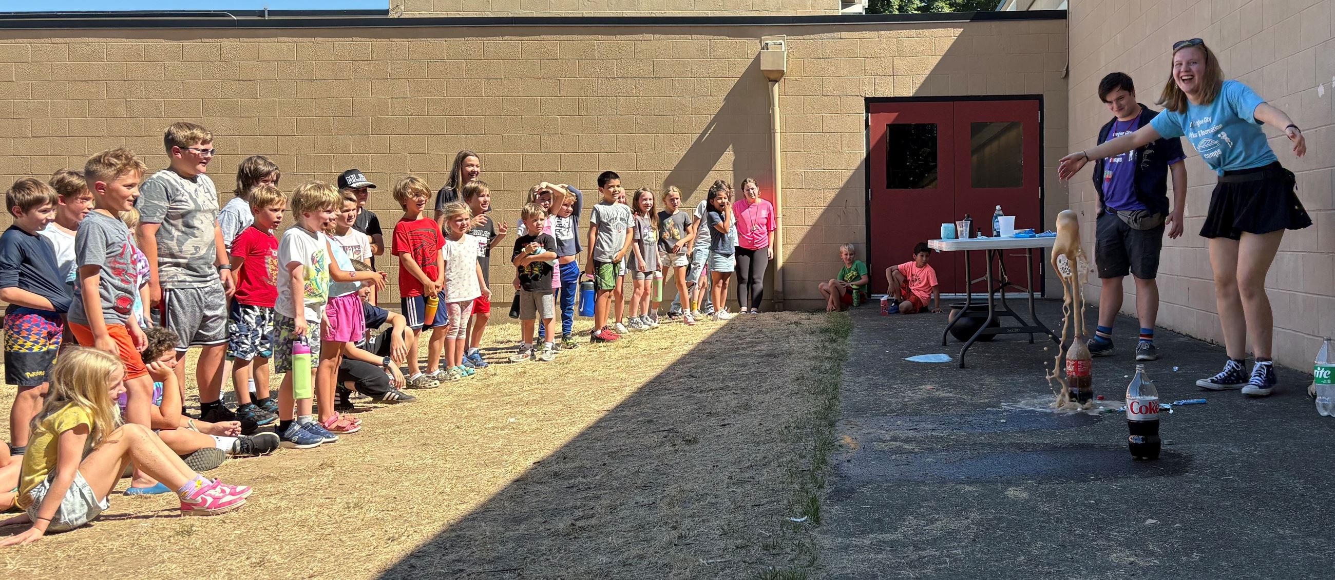 Group of children watching two camp counselors doing a science experiment.